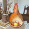 A rustic farmhouse table centerpiece showing a dried gourd finished with foliage artwork and battery-operated candle inside.